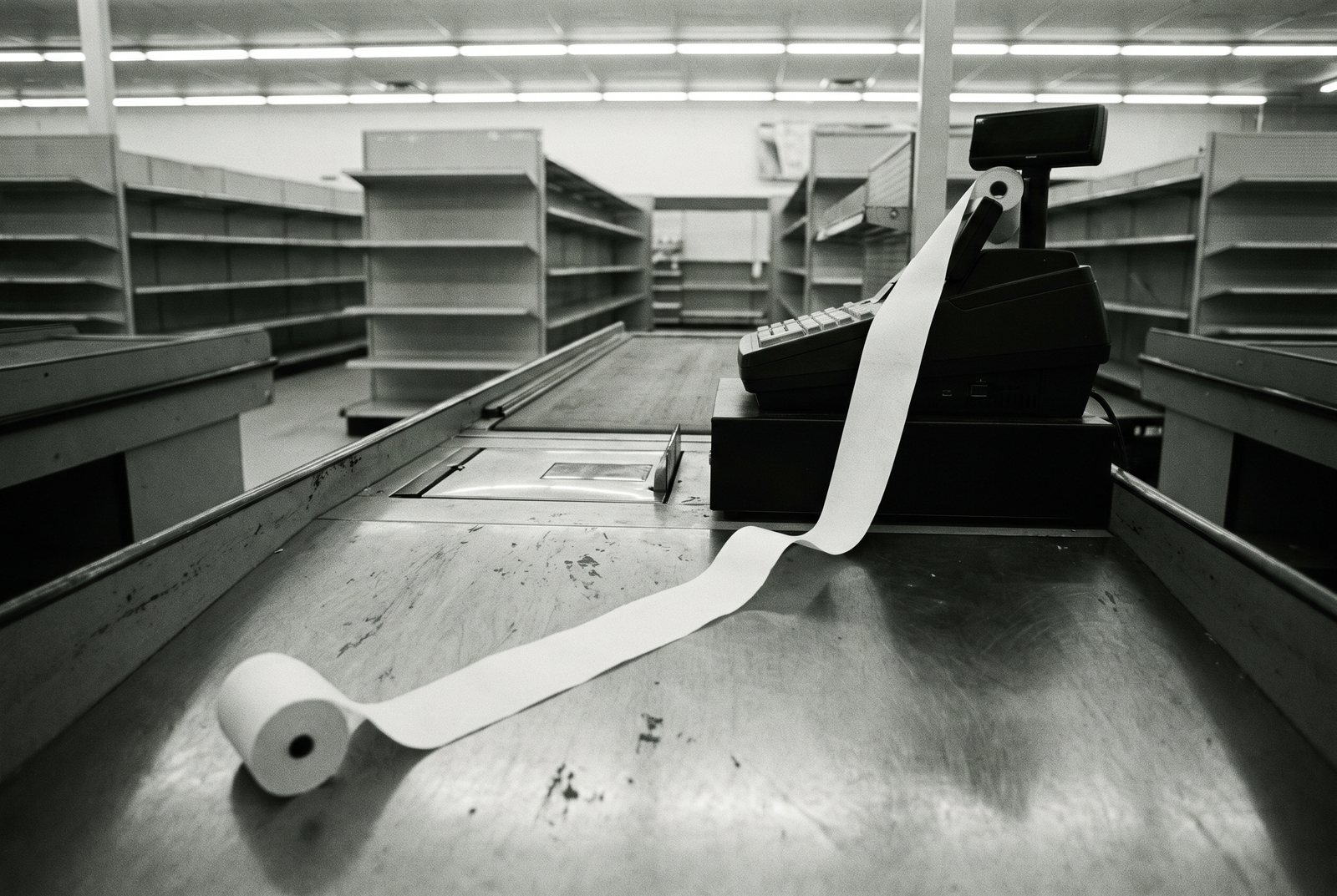 A blank receipt roll unspooled across an empty store counter and onto the floor.