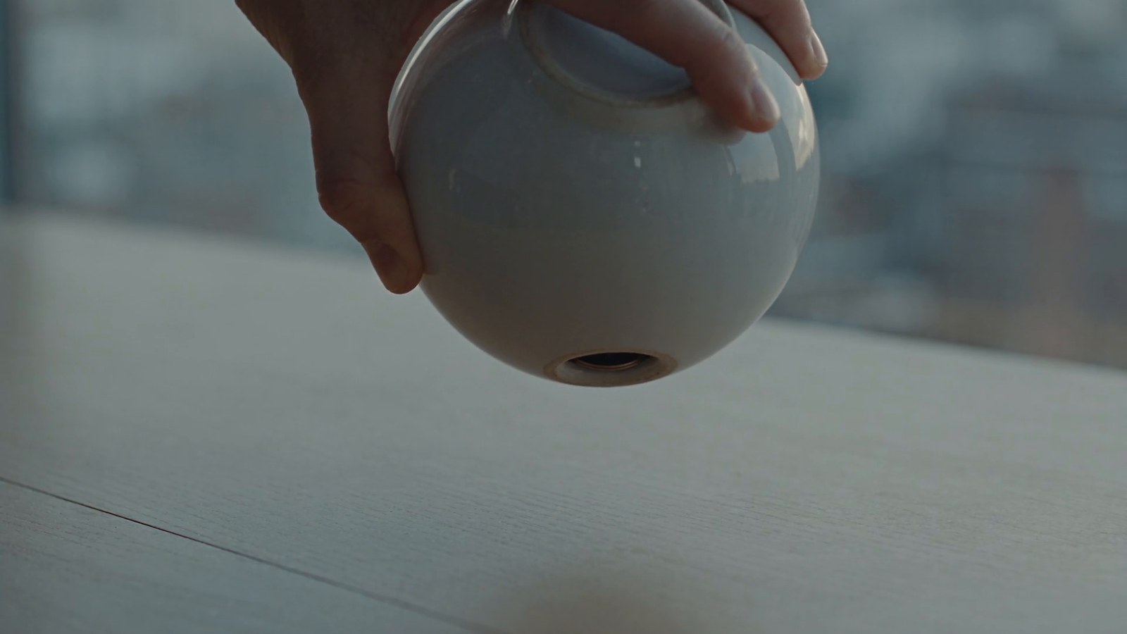 A ceramic piggy bank shaken upside down over a bare desk; one coin falls out.
